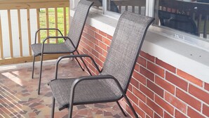 Two metal chairs with woven seats on a porch with a tiled floor and a brick wall. - Cozy Home Near I-4, Lakeland hospital, cancer center ＆ Joker Marchant Stadium (Lakeland)