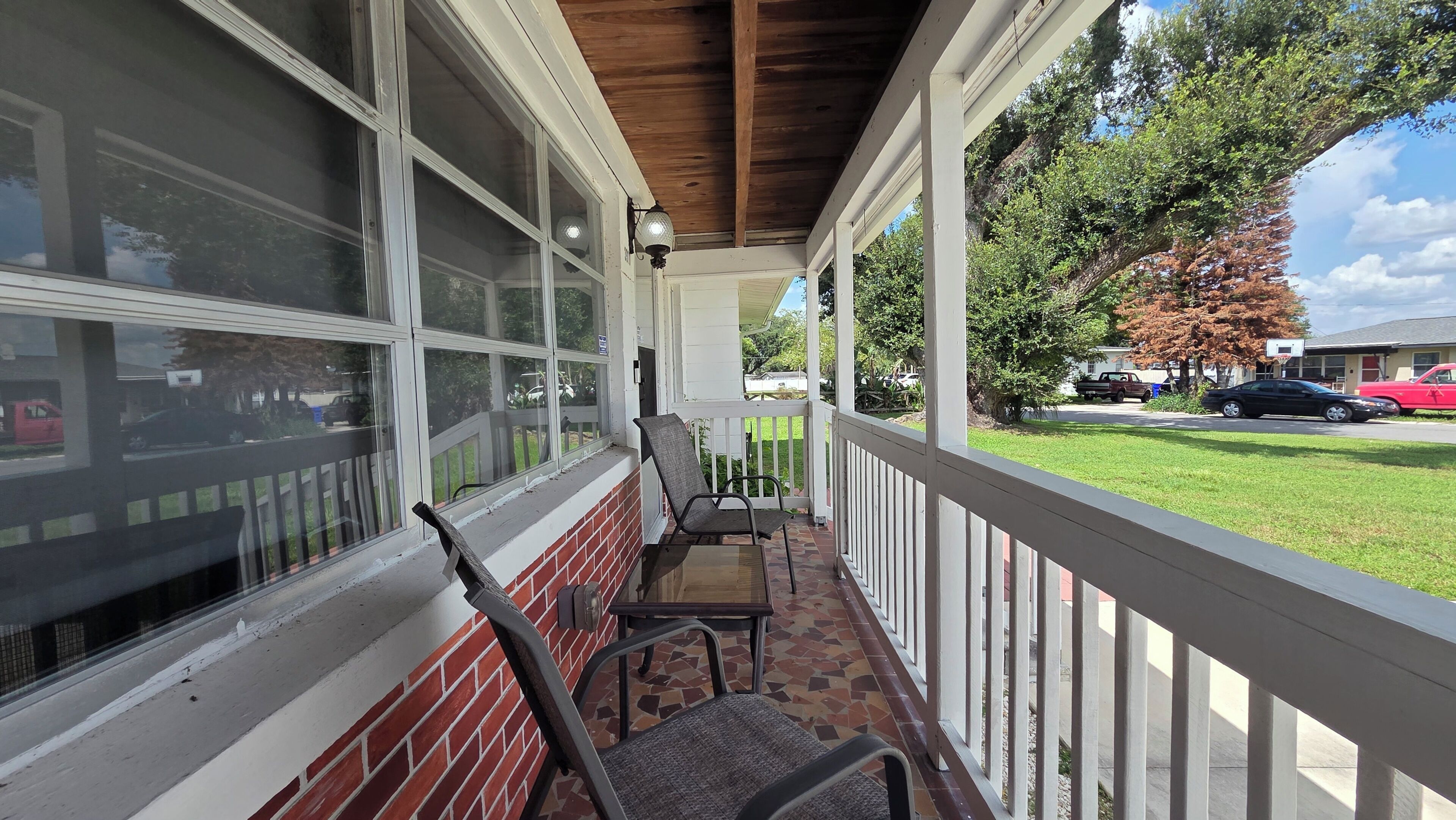 A covered porch with a brick wall, a wooden ceiling, and a view of a street with cars and trees.