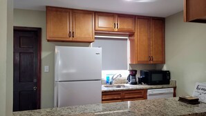 A kitchen with wooden cabinets, a white refrigerator, a black microwave, and a coffee maker. - Cozy Home Near I-4, Lakeland hospital, cancer center ＆ Joker Marchant Stadium (Lakeland)