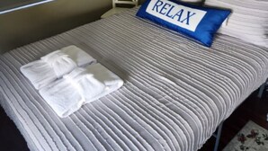 A neatly made bed with striped bedding, a blue pillow with the word "RELAX", and two folded white towels. - Cozy Home Near I-4, Lakeland hospital, cancer center ＆ Joker Marchant Stadium (Lakeland)