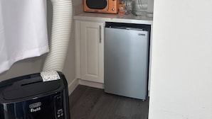 Kompakti keittiö, jossa on mikroaaltouuni, jääkaappi ja valkoiset kaapit.