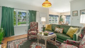 Een woonkamer met een groene bank, een fauteuil met bloemenprint en een vloerkleed met een patroon.