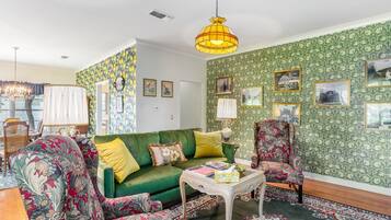 Relax in this inviting space with a green sofa, armchair, and coffee table, surrounded by framed pictures and a chandelier.