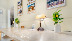 Een houten tafel met een lamp, een vaas met een plant en ingelijste foto's aan de muur.