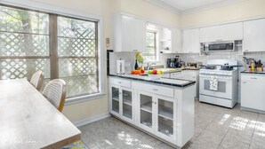 Een moderne keuken met witte kastjes, een centraal kookeiland en een eethoek met tafel en stoelen.