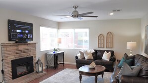 Una sala de estar con chimenea, televisor de pantalla plana, ventilador de techo, sofá y mesa de centro.