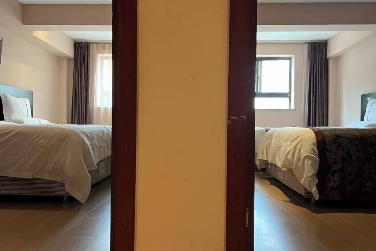 A hotel room with two beds, a wooden floor, and a window.
