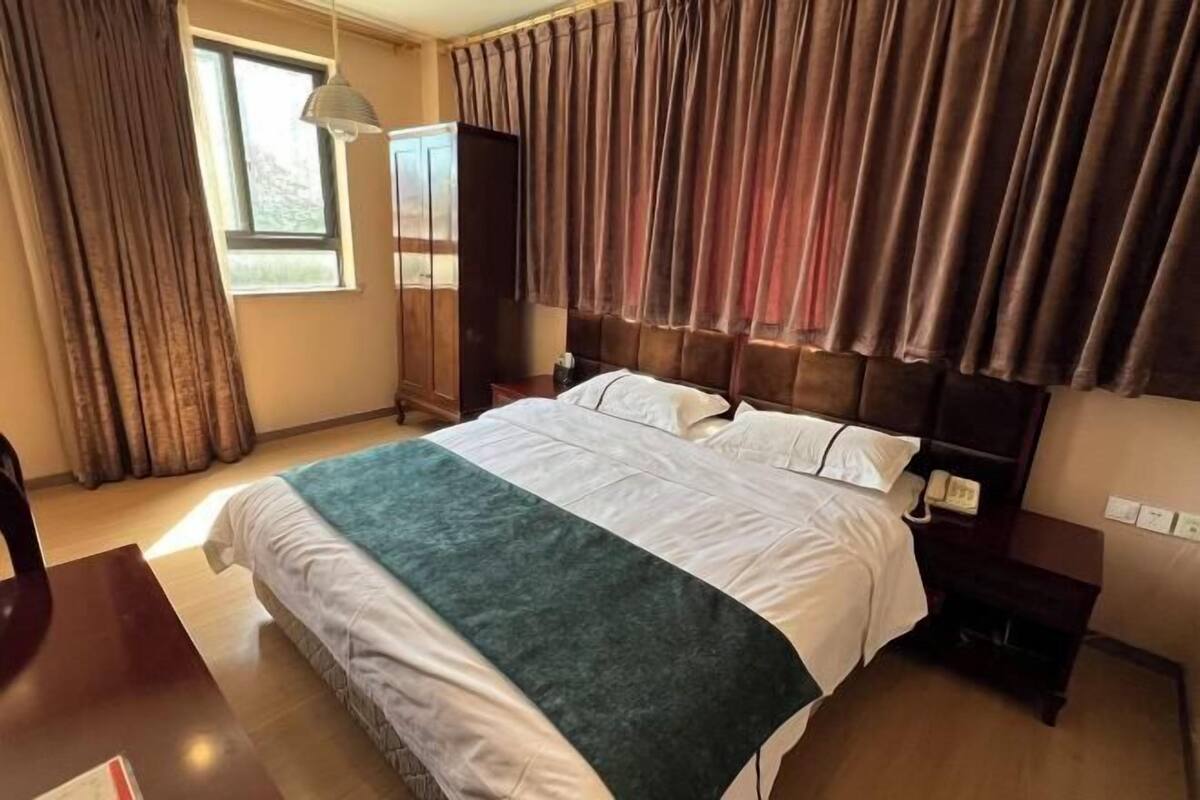 A hotel room with a large bed, a wardrobe, a desk, and a window with curtains.