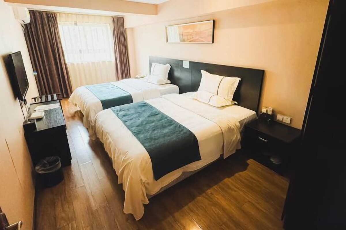 A hotel room with two beds, a TV, a desk, and a window with curtains.