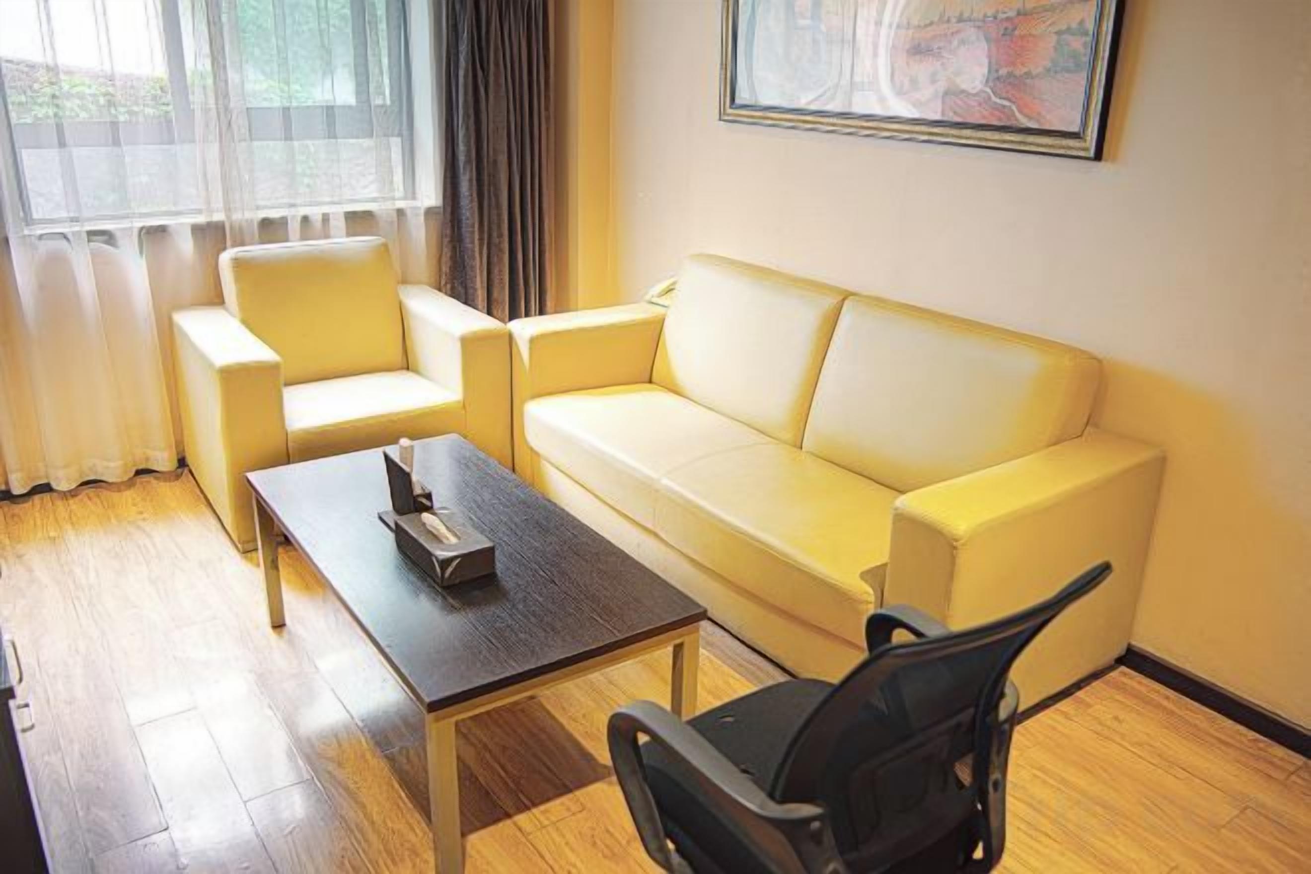 Une pièce avec un canapé jaune, une chaise noire, une table basse en bois et une fenêtre avec des rideaux.