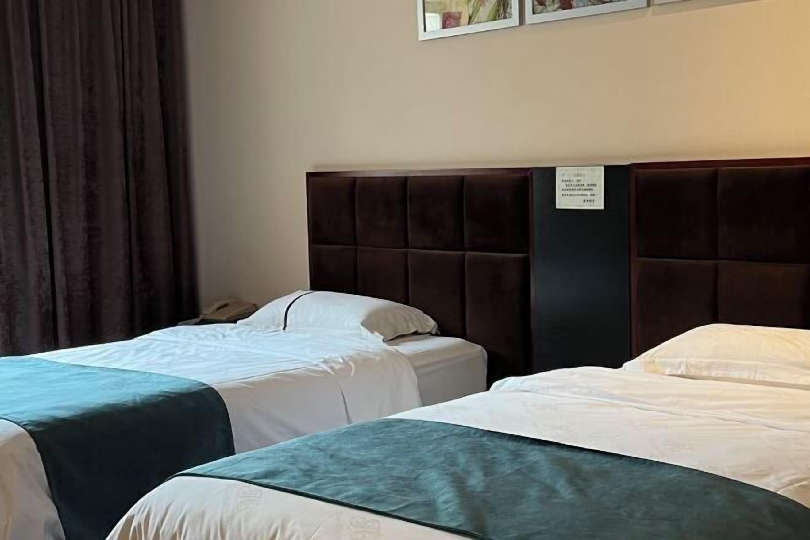 A hotel room with two beds, a dark headboard, a white wall, and a sign with text.