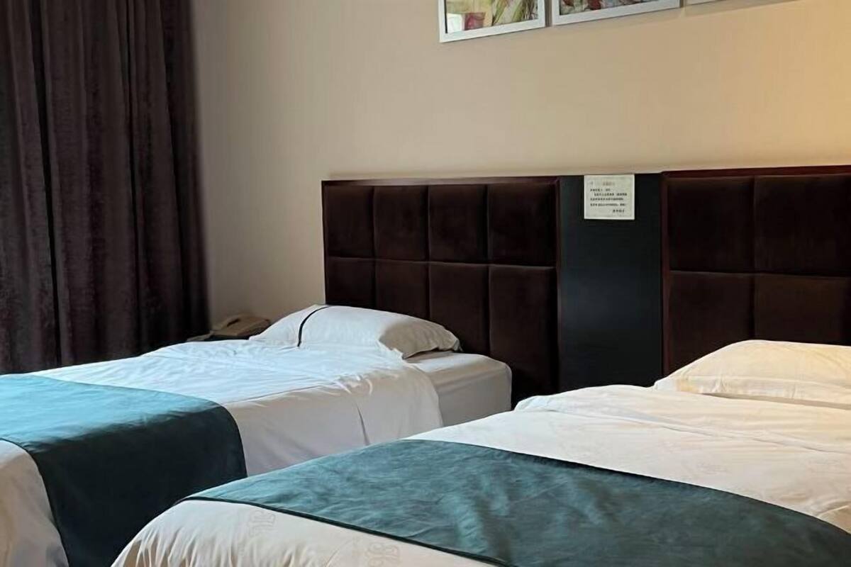 A hotel room with two beds, a dark headboard, a white wall, and a sign with text.