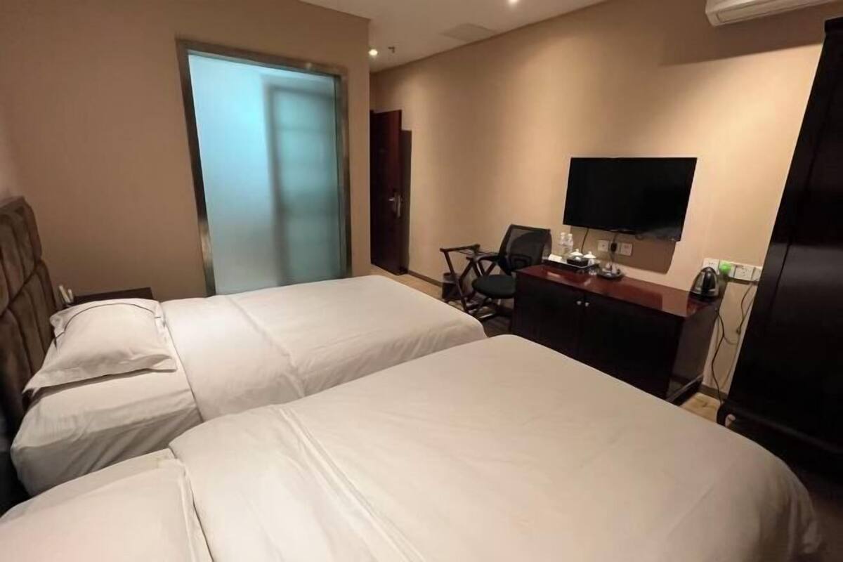 A hotel room with two beds, a desk with a chair, a television, and a door.