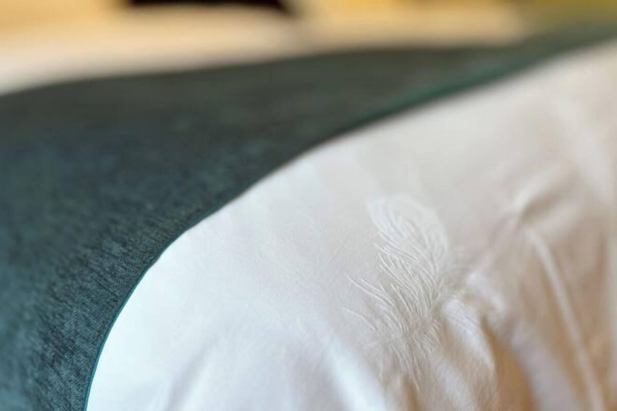 A close-up of a bed with a white sheet and a dark green headboard.
