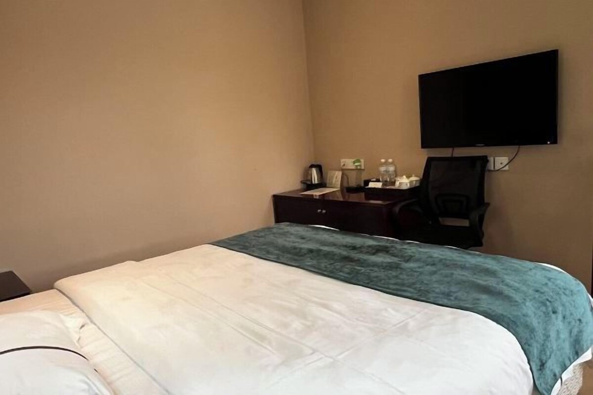 Habitación de hotel con cama, escritorio, silla, televisor de pantalla plana y televisor montado en la pared.