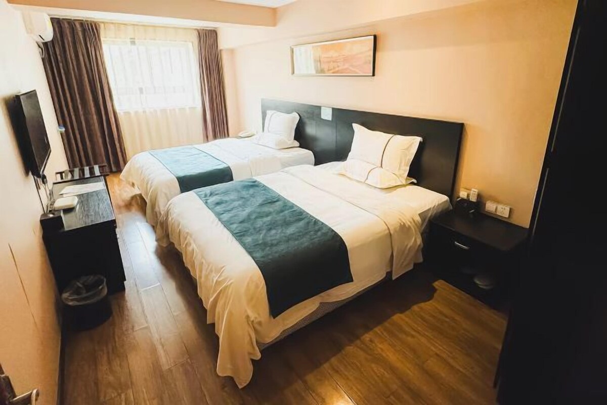 Habitación de hotel con dos camas, televisión, escritorio y ventana con cortinas.
