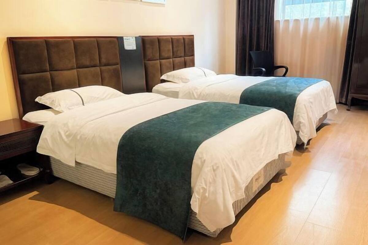 A hotel room with two beds, a wooden headboard, a chair, and a wooden floor.