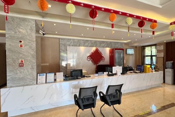 A hotel reception area with a marble counter, black chairs, and red decorative elements. - Dinghui Holiday Hotel (Chongqing)