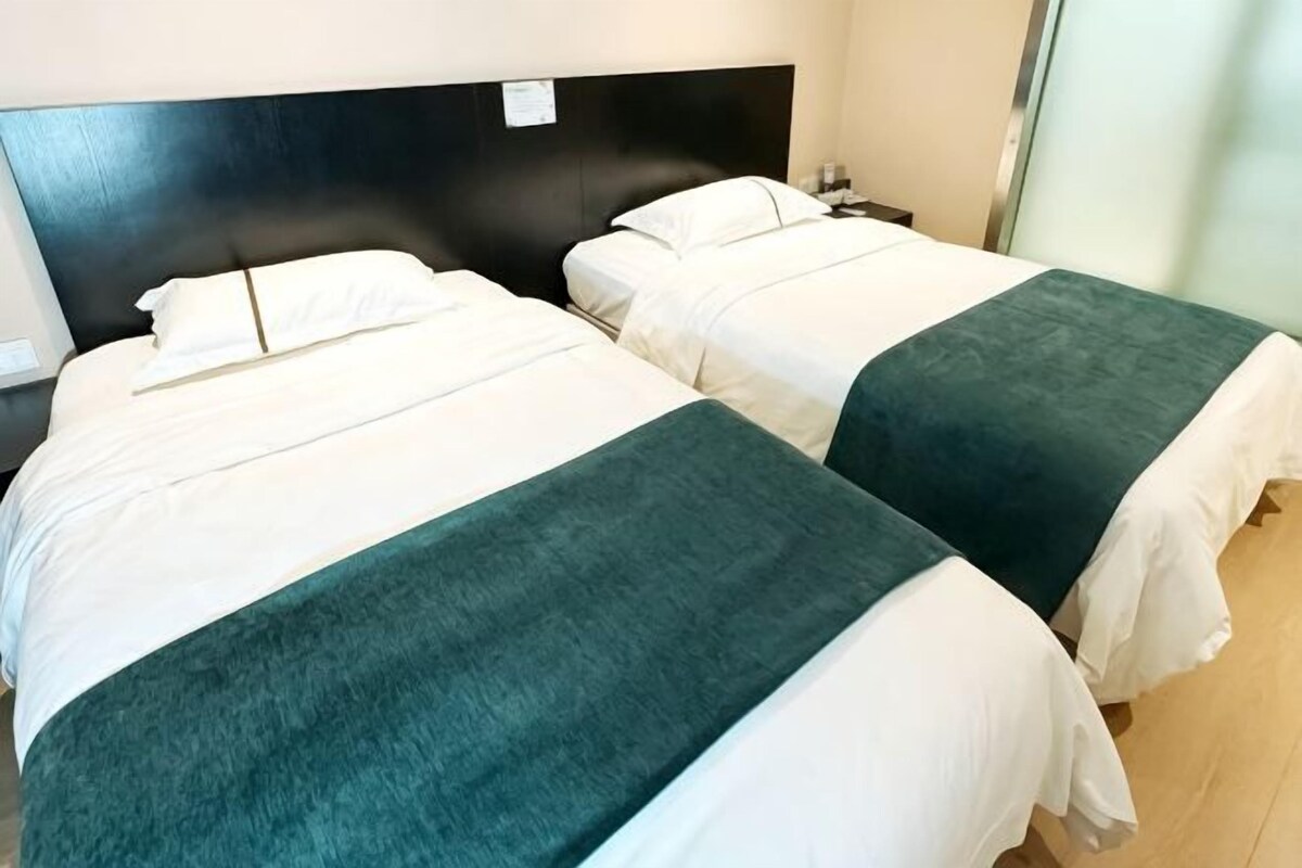 Two twin beds with white linens and green throw blankets, a black headboard, and a wooden floor.