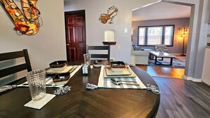 A dining area with a dark wooden table set for four, including plates, cutlery, and glasses. A decorative saxophone wall art is visible. - Cozy 1-bedroom apartment in lovely St. Louis with WiFi, AC (St. Louis)