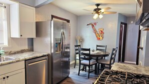 A compact kitchen with a stainless steel refrigerator, a gas stove, and a dining area with a table and chairs. - Cozy 1-bedroom apartment in lovely St. Louis with WiFi, AC (St. Louis)