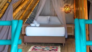 Una habitación con una cama bajo un techo de bambú, una lámpara colgante y suelo de madera.