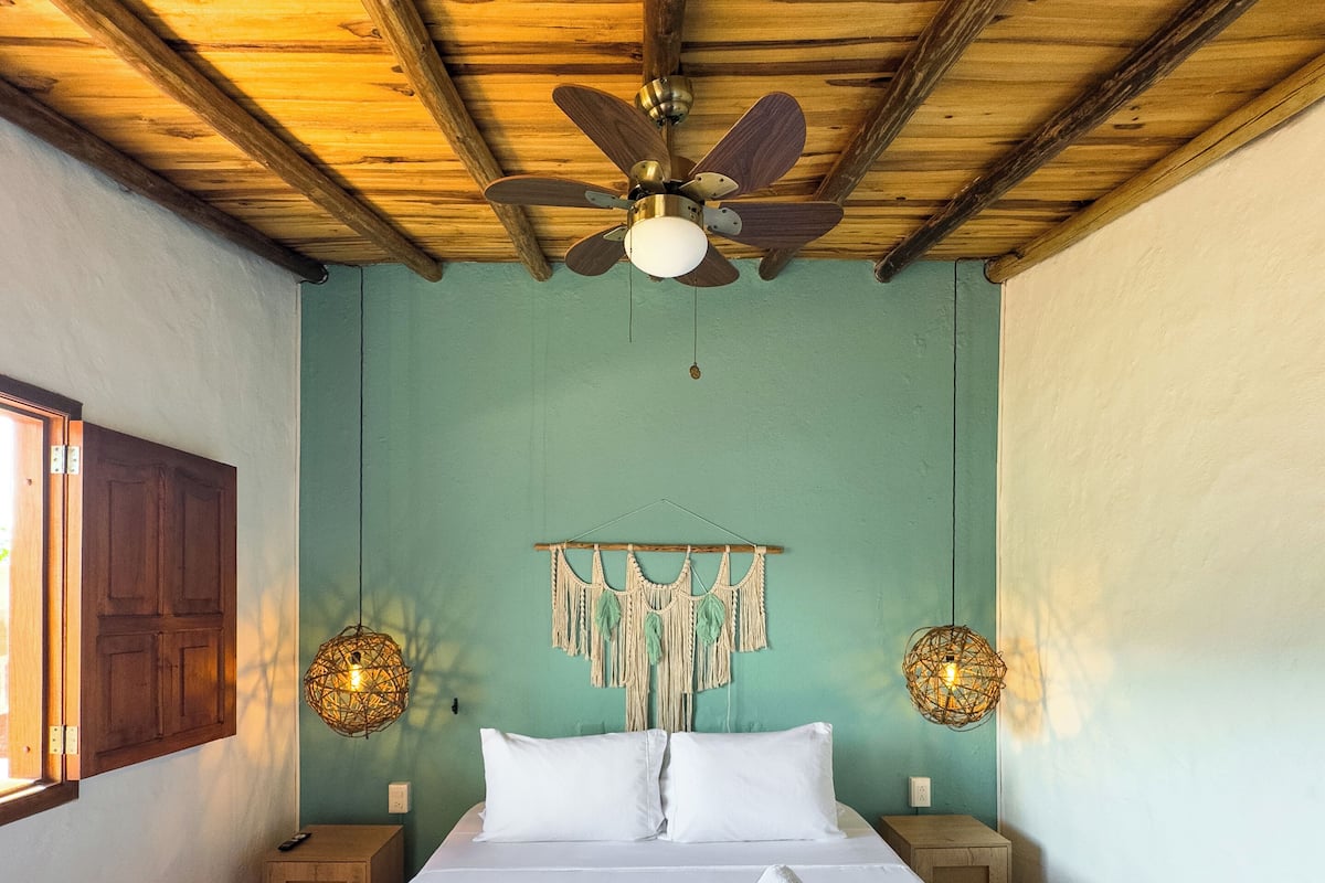 A bedroom with a wooden ceiling, a bed with white bedding, a ceiling fan, and two wall-mounted lamps.