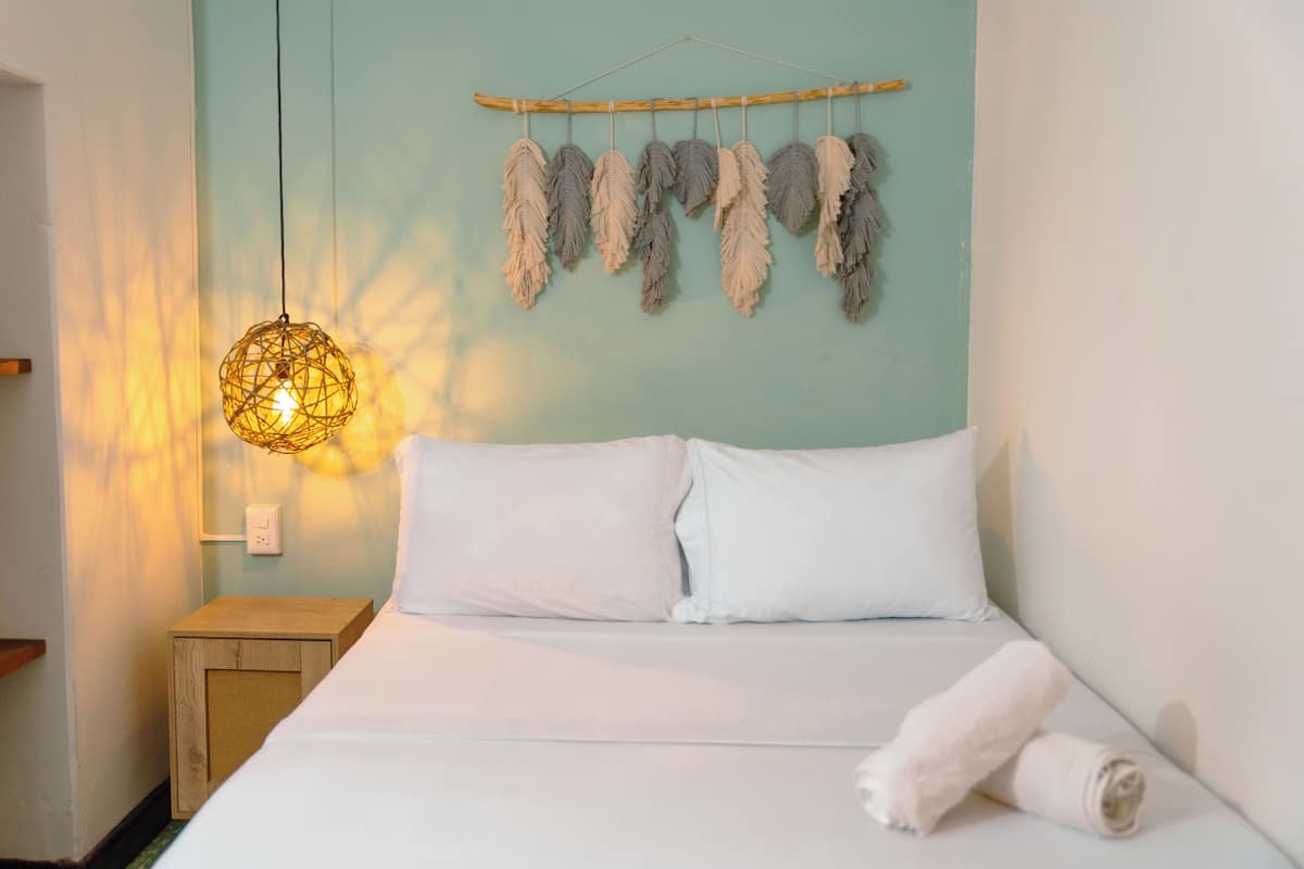 A neatly made bed with white linens, a hanging light fixture, and a wall-mounted decorative item.