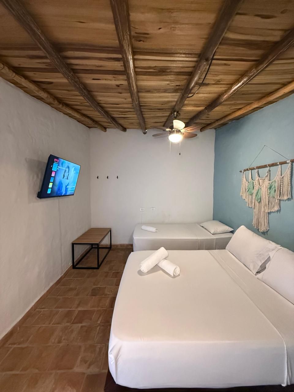 A hotel room with two beds, a television mounted on the wall, a ceiling fan, and a small table.