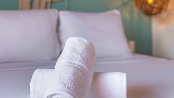 Una cama bien hecha con ropa blanca, una pared con un adorno de macramé y una lámpara colgante.