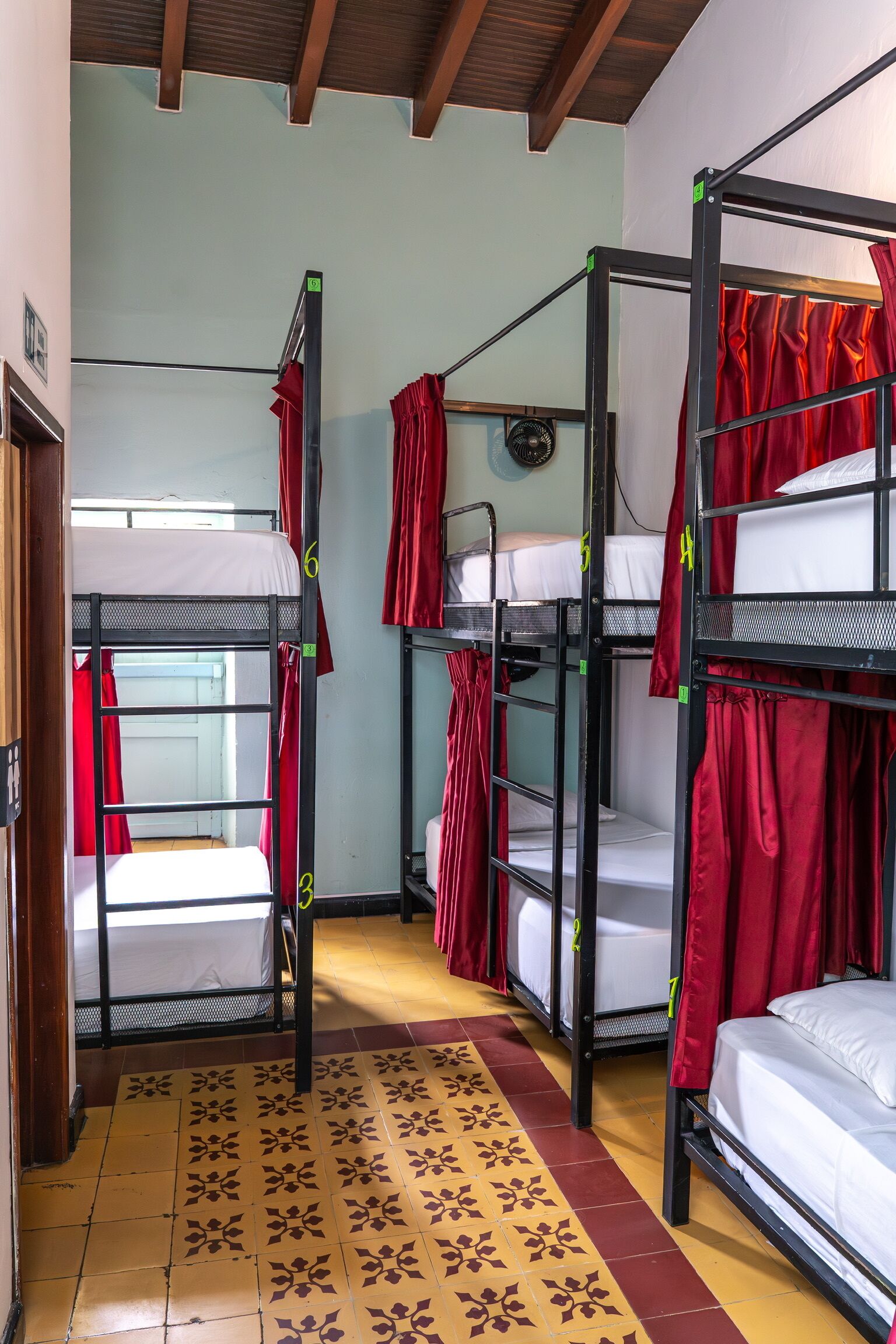 A dormitory room with bunk beds, red curtains, and patterned floor tiles.