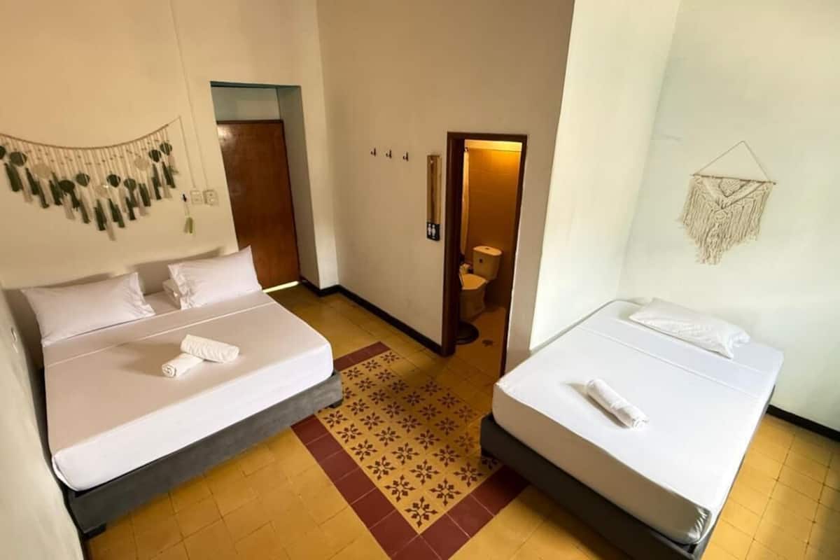 A hotel room with two beds, a patterned rug, a wall hanging, and a door leading to a bathroom.
