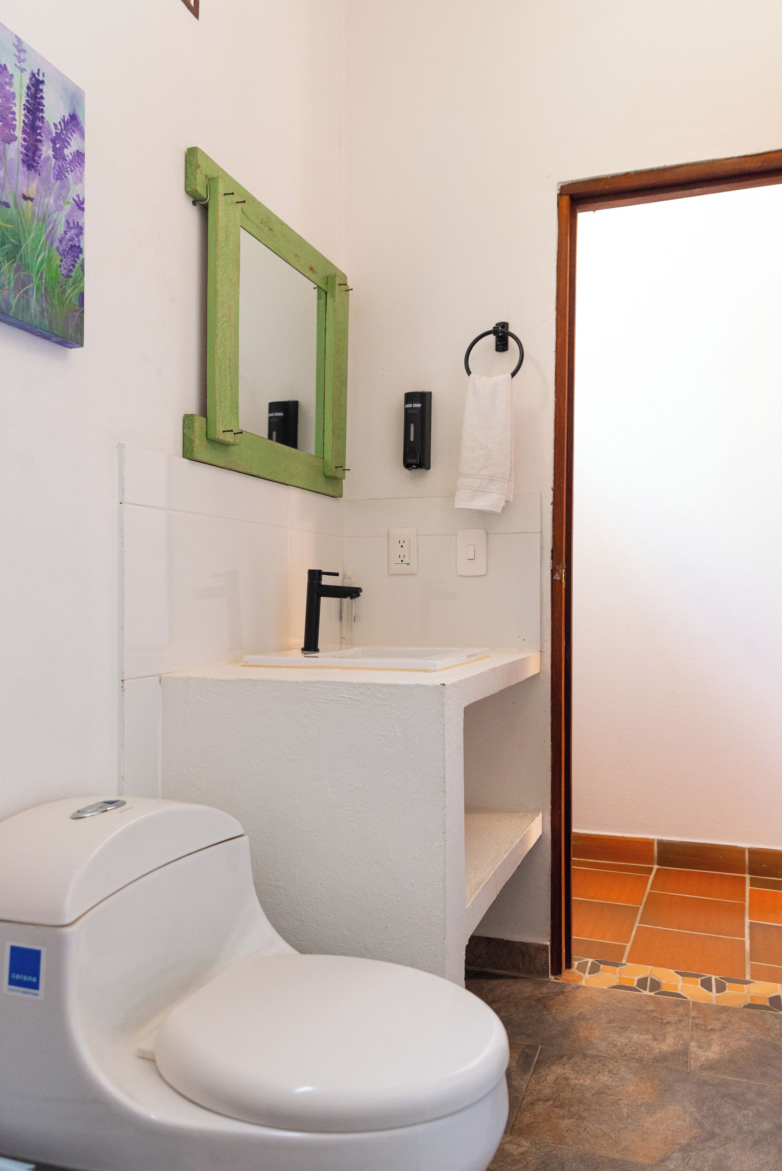 A bathroom with a white toilet, a green-framed mirror, a white sink, and a towel rack.