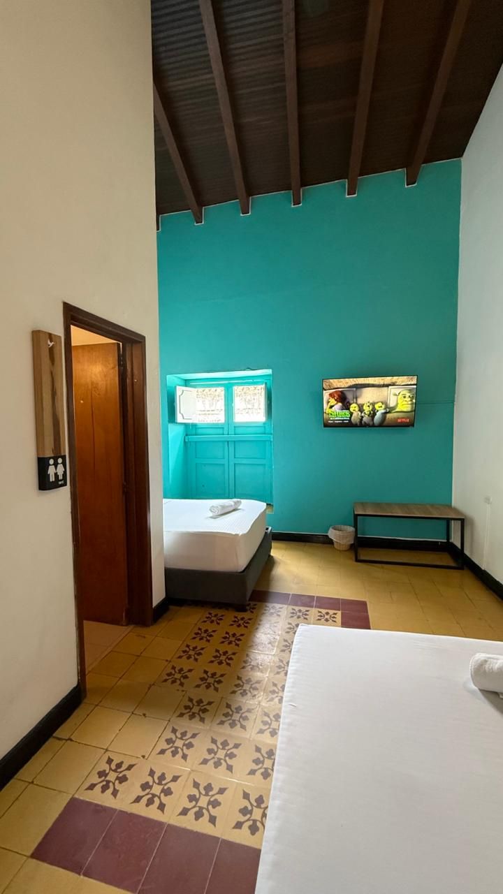 A room with a bed, a bench, a window with curtains, a wall-mounted TV, and a door.