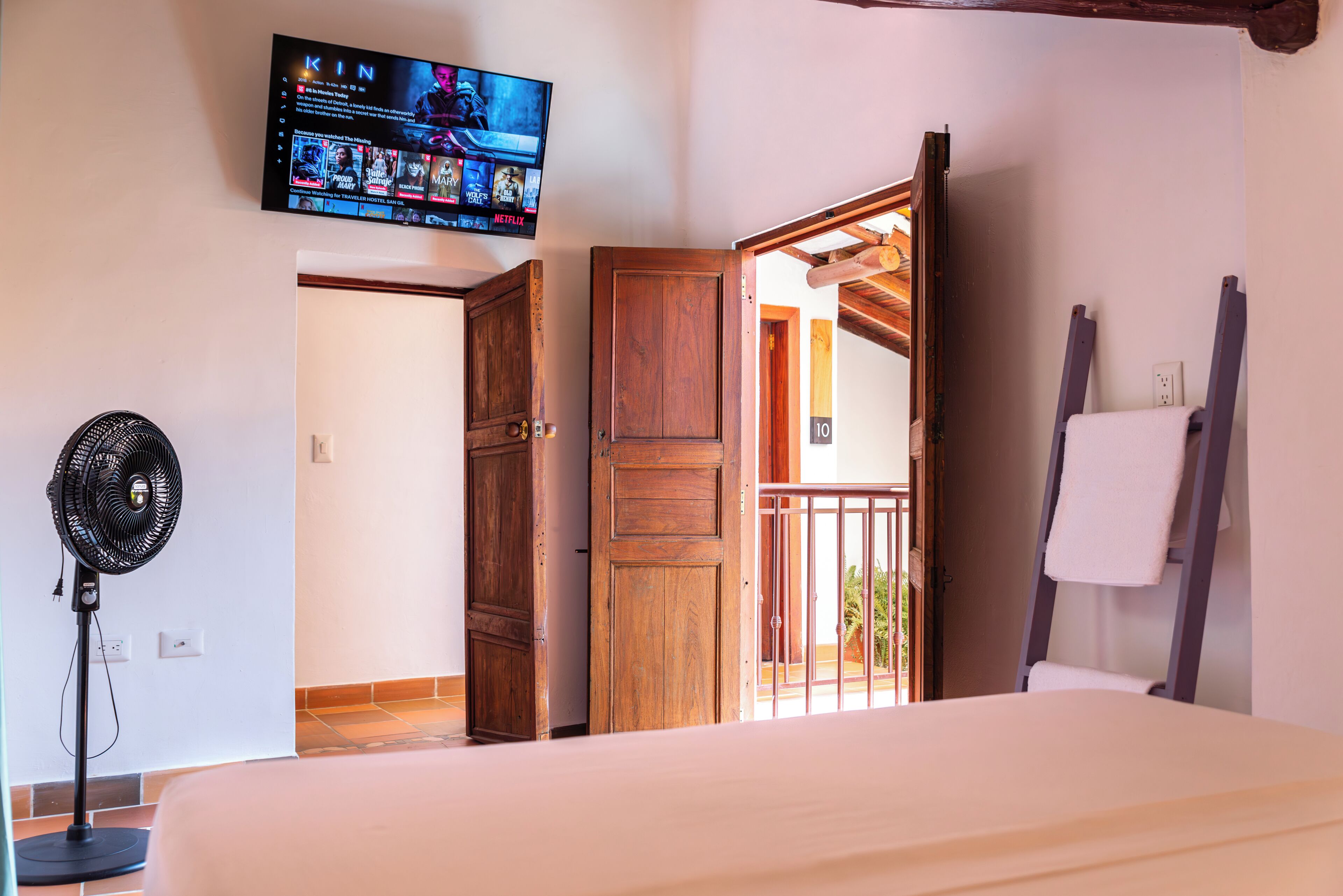 Un dormitorio con cama, televisor montado en la pared, puerta de madera y ventilador.