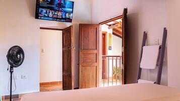 Un dormitorio con cama, televisor montado en la pared, puerta de madera y ventilador.