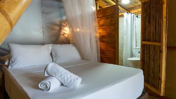 A bed with white linens and a rolled towel, a wooden ceiling, and a wooden wall.