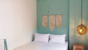 A bedroom with a bed, a wooden headboard, a macrame wall hanging, a hanging light fixture, and a small wooden cabinet.