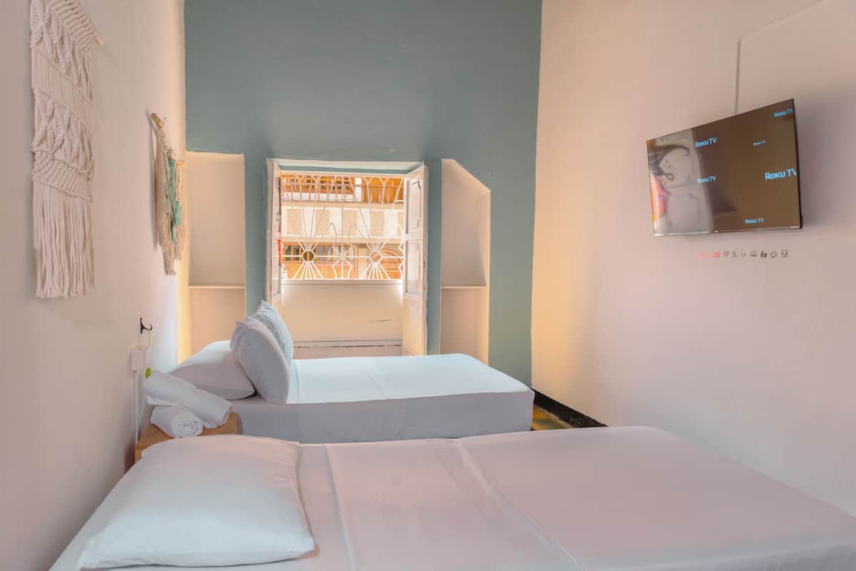 A hotel room with two beds, a TV on the wall, and a window with a view of the interior.
