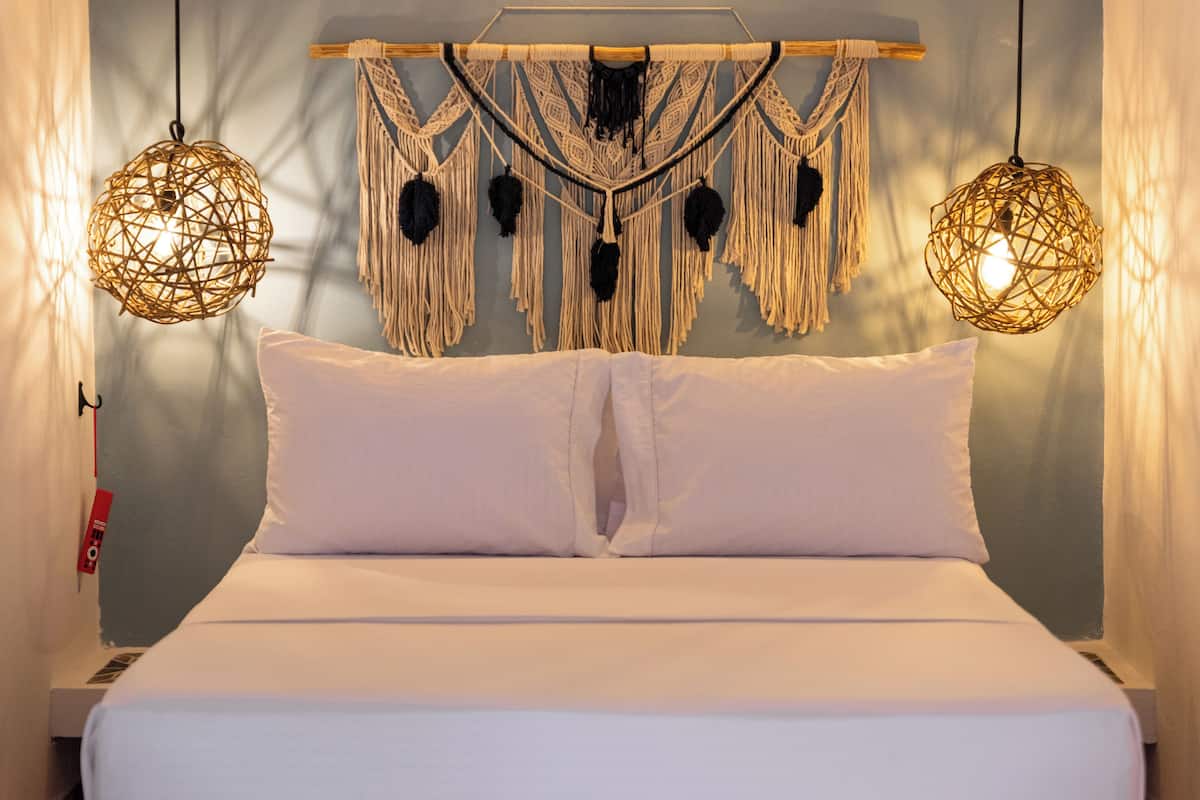 A bed with white linens, a macrame wall hanging, and two spherical woven light fixtures.
