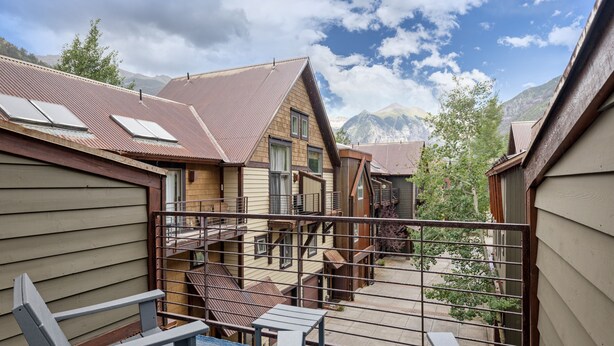 A residential building with a balcony, a staircase, and a view of mountains.