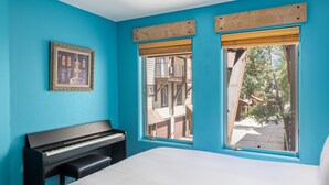 A room with a bed, a piano, and two windows with wooden shutters.