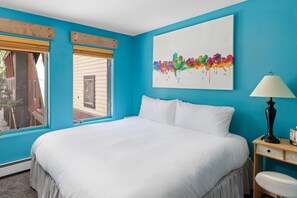 A bedroom with a large bed, a window, a painting, and a nightstand.