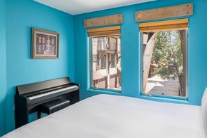 A room with a bed, a piano, and two windows with wooden frames.