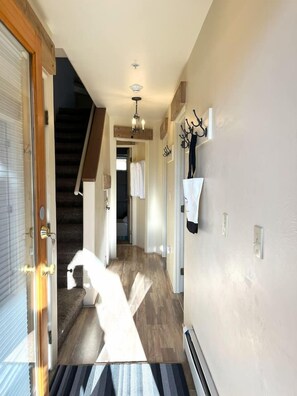 A hallway with a wooden floor, a staircase, and a door leading to a room.