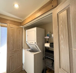 A laundry room with a front-loading washer and dryer, wooden doors, and a shelf with folded towels.