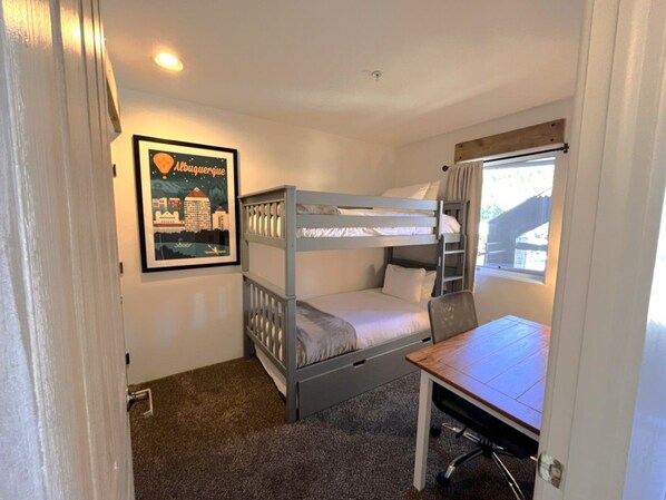 A room with a bunk bed, a desk, and a window with curtains.