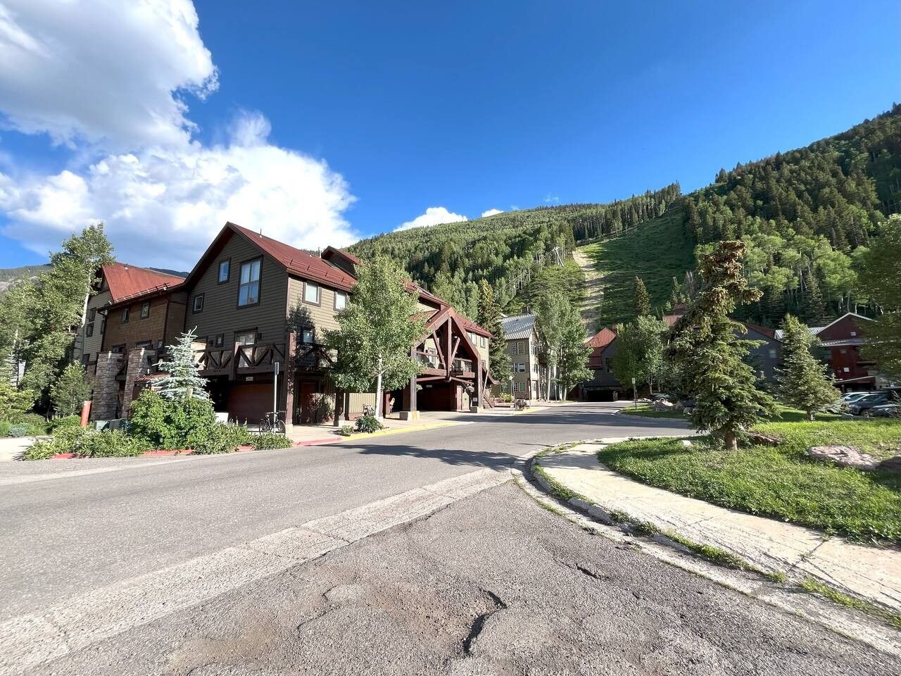 Une rue résidentielle bordée de maisons, un ciel dégagé et un paysage vallonné en arrière-plan.