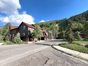 A residential street with houses, a clear sky, and a hilly landscape in the background.
