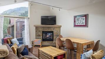 Un salon chaleureux avec une cheminée, un téléviseur fixé au-dessus, et un coin repas avec des meubles en bois.